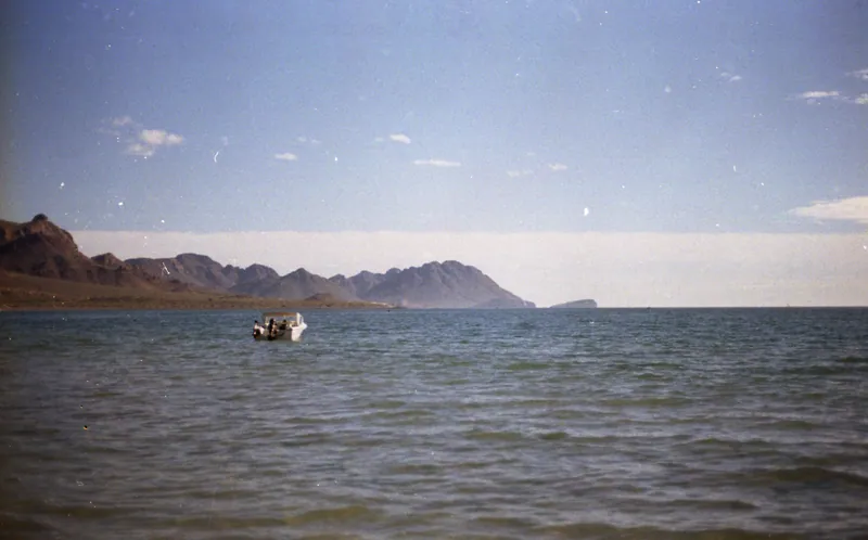 A small boat crossing calm water beneath distant mountains
