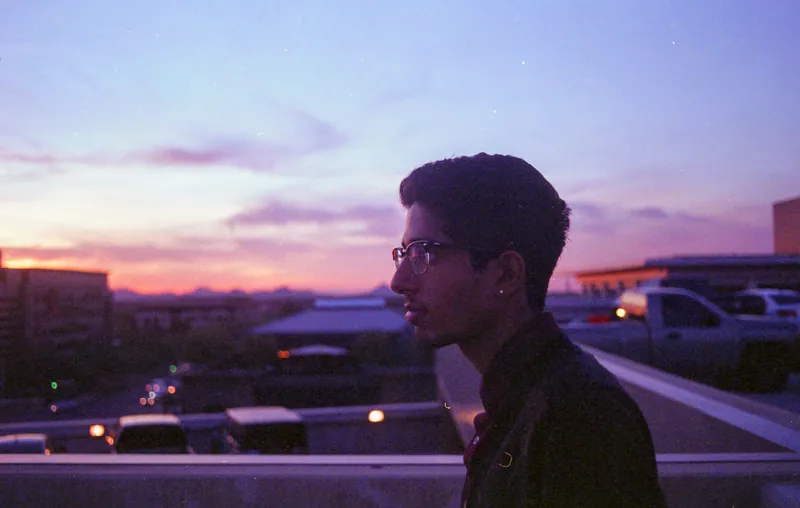 A person in profile on a rooftop beneath a violet sunset