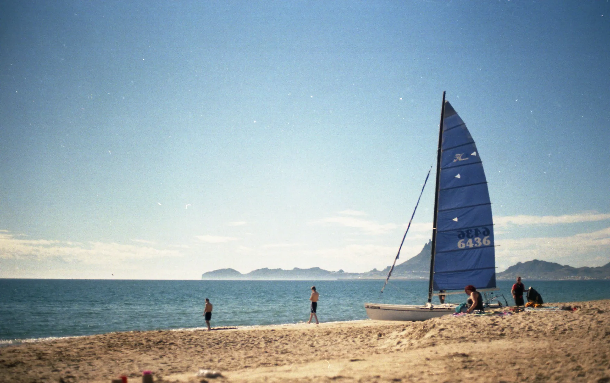 A sailboat framed by pale water and distant hills.